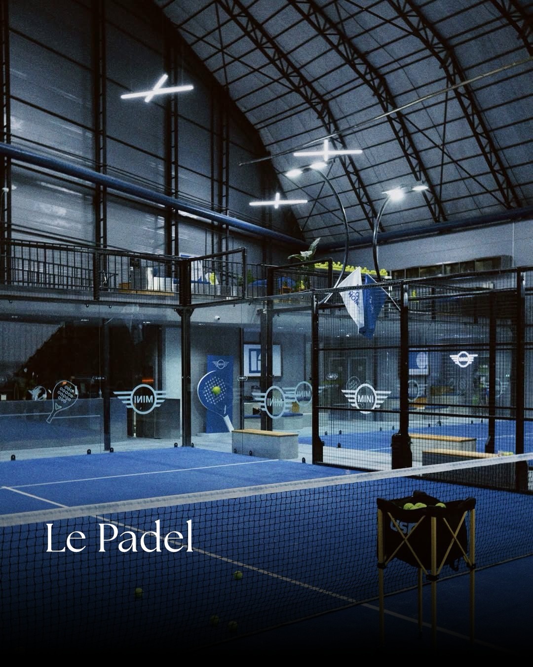 Kapalı Le Padel kortunda mavi zemin, file ve cam duvarlar.